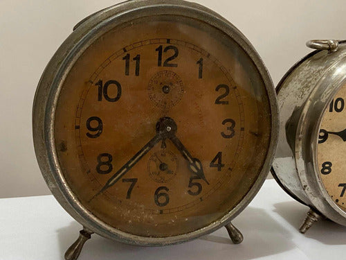 Vintage silver-colored alarm clock with aged dial and classic numbers on a white surface