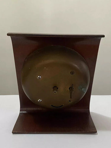 Back view of an antique wooden table clock with a metal wind-up mechanism and a curved base.